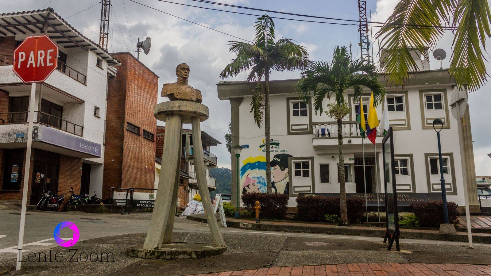 Una esquina de la plaza donde hay una escultura de Simón Bolívar y en la otra esquina una estación de policia con un par de banderas en frente