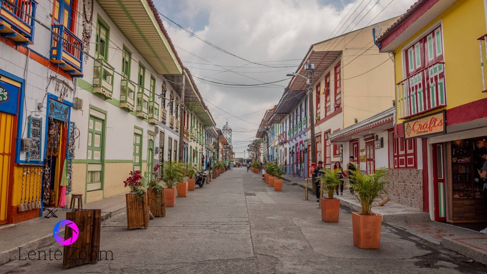 Calle decorada con plantas en macetas un poco grandes y llena de casas típicas de diferentes colores