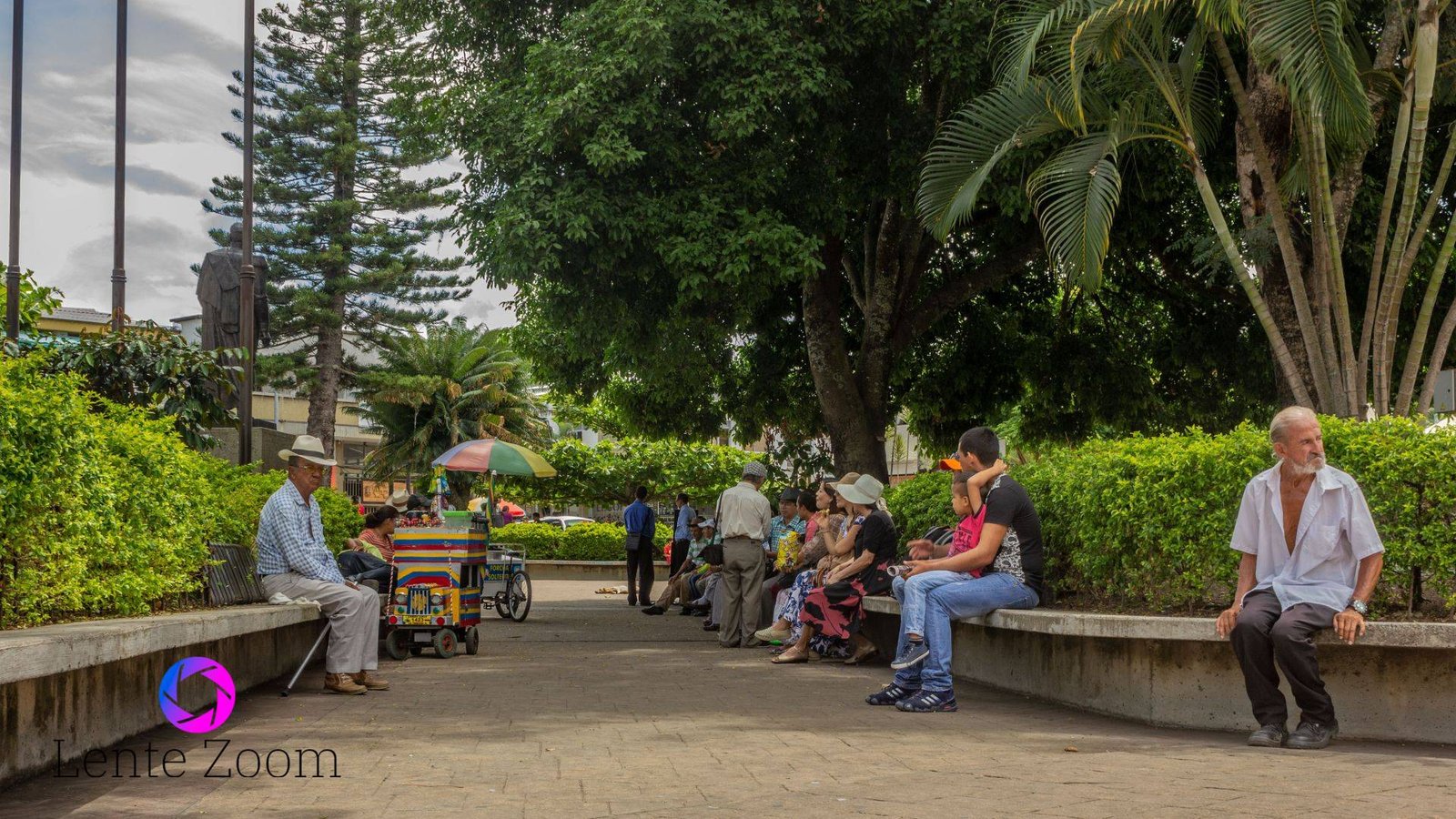 Varias personas sentadas en los bordes de los arbustos que hay en la plaza